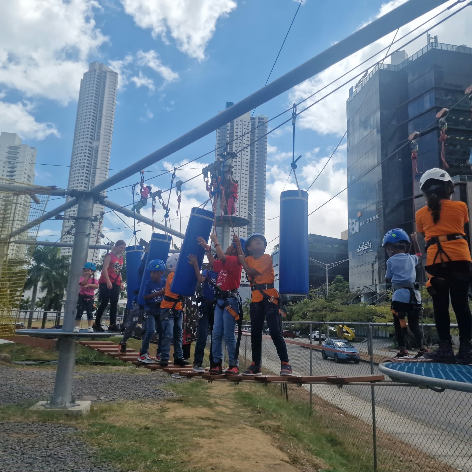 Niños con casco y arnés cruzando un puente colgante en el Playground de Cuerdas de Climb